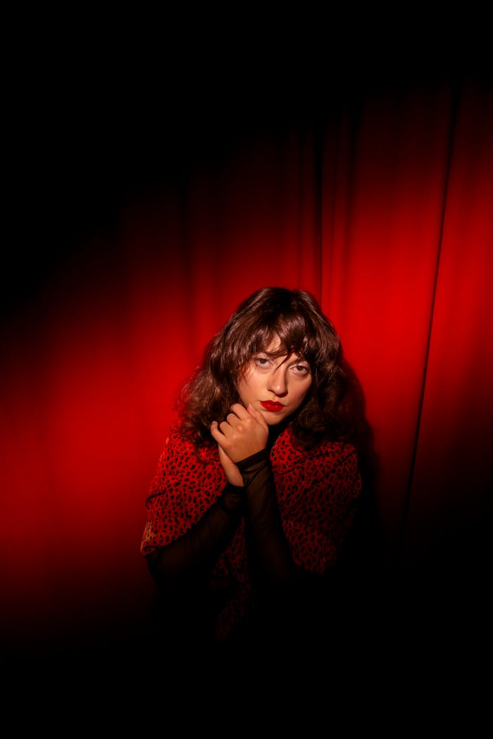 A striking portrait of a woman against a rich red background, exuding drama and emotion.